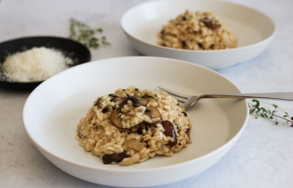 bowl of mushroom risotto with plate of parmesan in the background. 