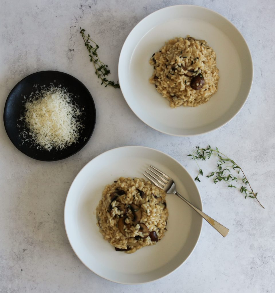 Two bowls of risotto next to a plate of parmesan. 