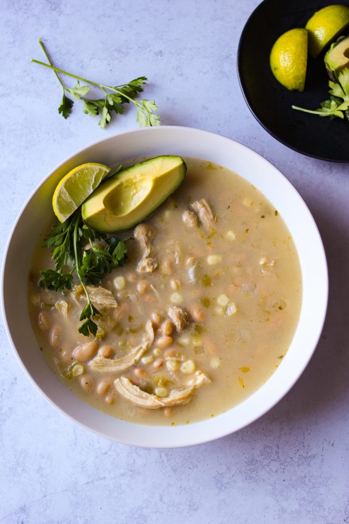 Top view of ranch white chicken chili in a white bowl next to a plate of lime and cilantro.