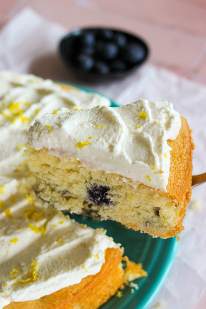 Slice of blueberry cake being taken out of the whole cake. 