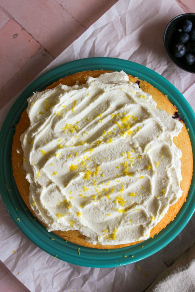 Blueberry cake on a blue plate with whipped cream and lemon zest on top. 