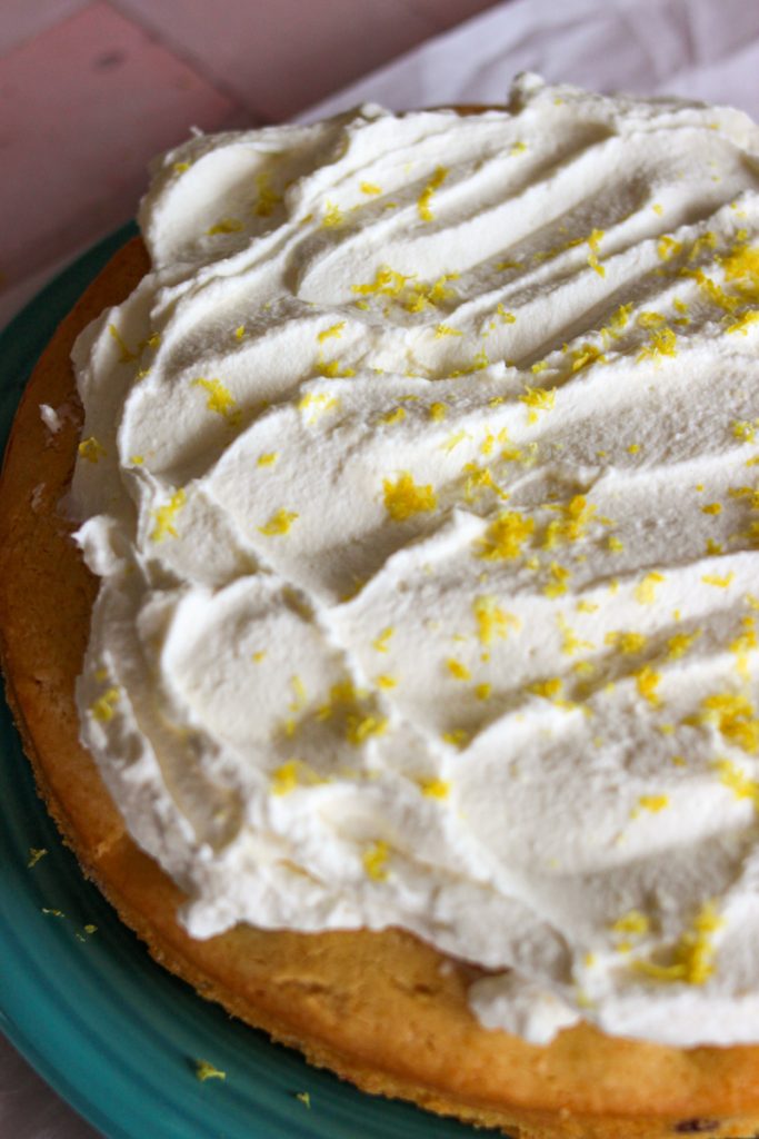 Close up of blueberry lemon sour cream cake with whipped cream and lemon zest on top. 