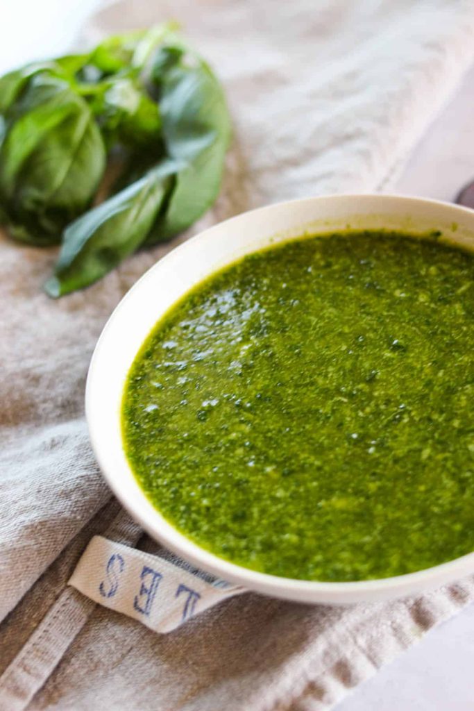 Pesto in a small white bowl on top of a kitchen towel. 