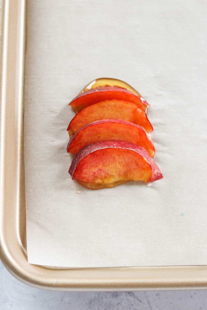 Peach slices on top of honey on parchment paper that is on a baking sheet. 