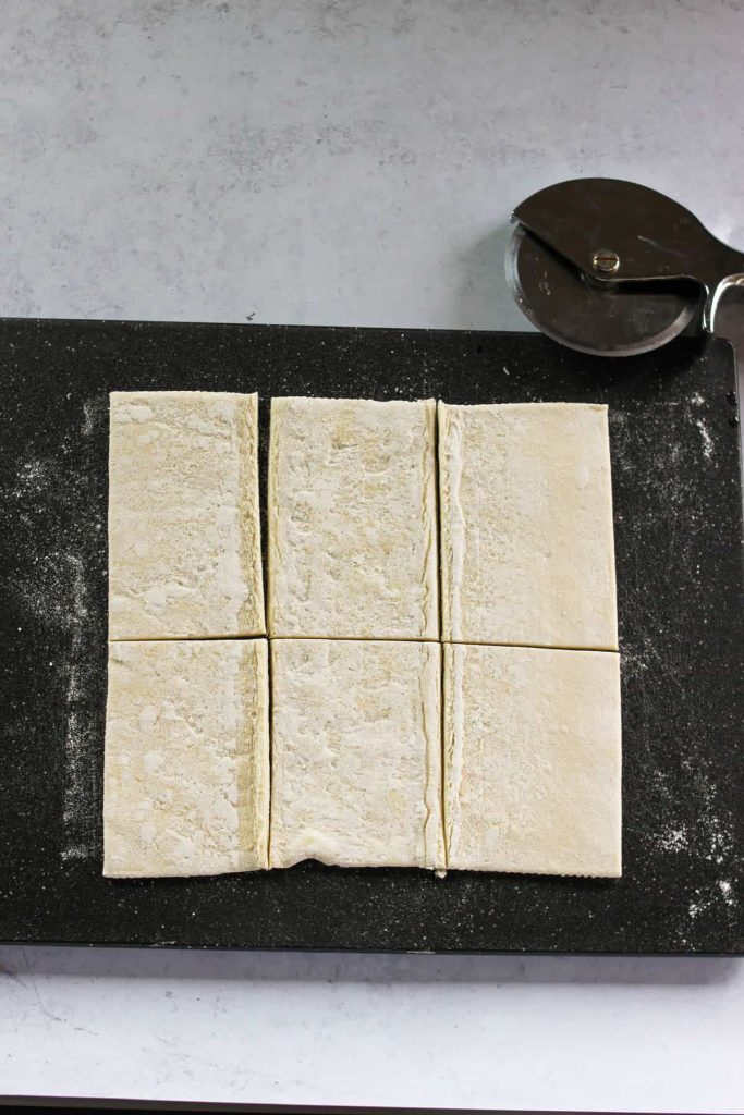 Puff pastry sheet on a cutting board, cut into six squares. 