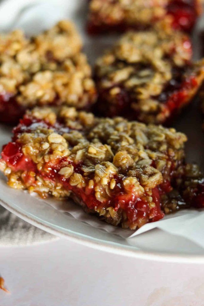 Strawberry oatmeal bar on a white plate lined with parchment with more bars in the background. 