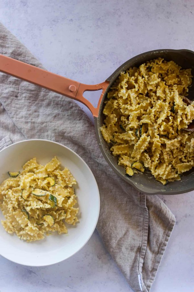 Bowl of creamy pasta next to a large skillet with more pasta in it. 