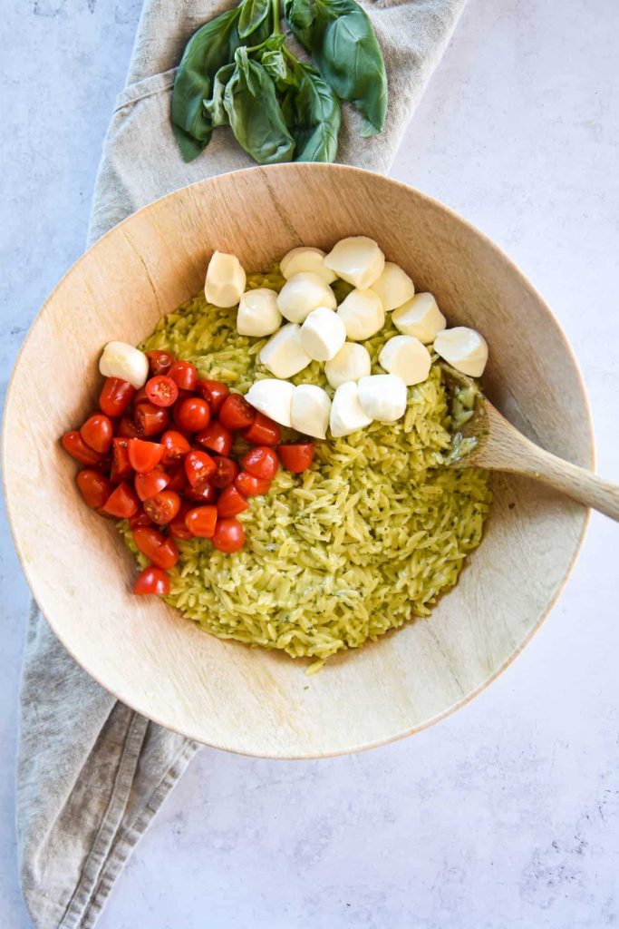 Pesto orzo in a serving bowl with tomatoes and mozzarella pearls. 