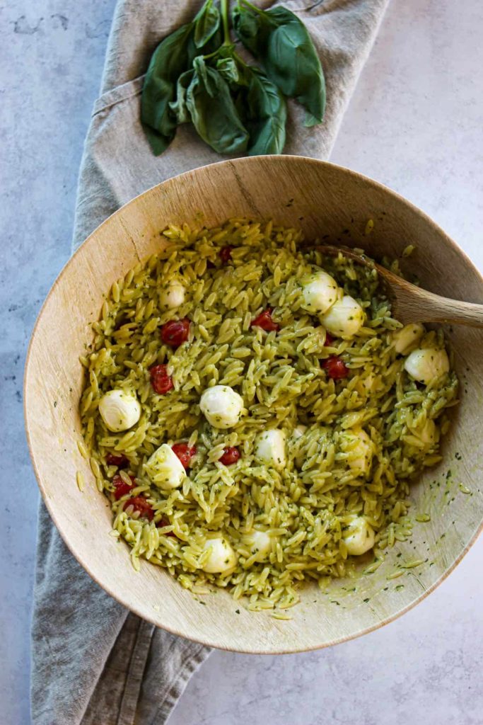 Pesto orzo with tomatoes and mozzarella in a wooden serving bowl. 