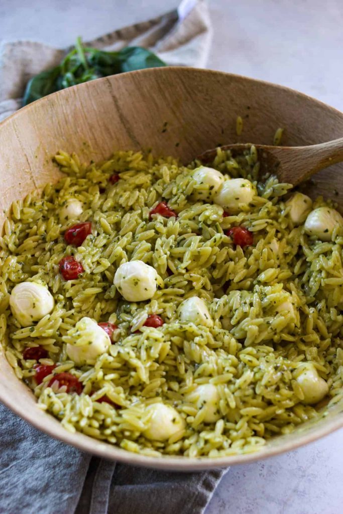 Pesto orzo after being mixed in a mixing bowl with a wooden serving spoon. 