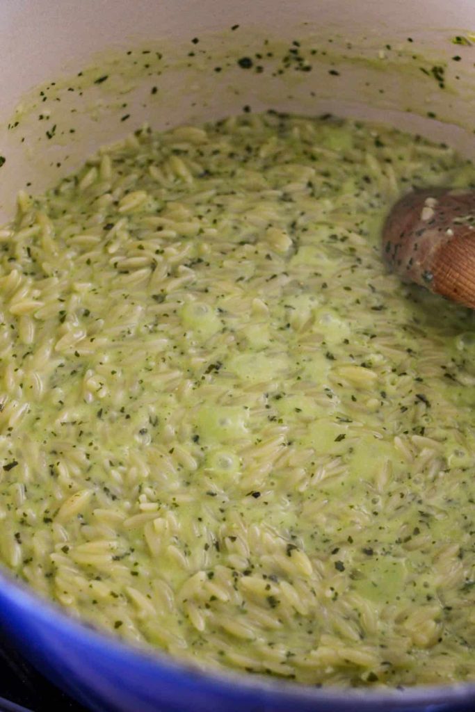 Orzo in a dutch oven being mixed with cream and cheese with a wooden spoon. 