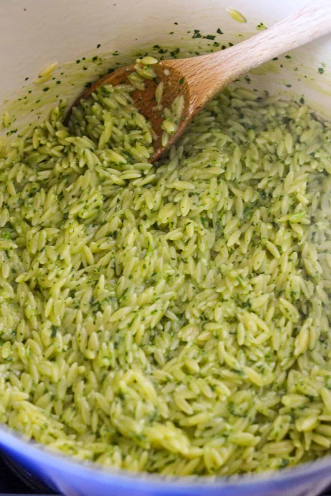 Orzo in a dutch oven being mixed with pesto. 