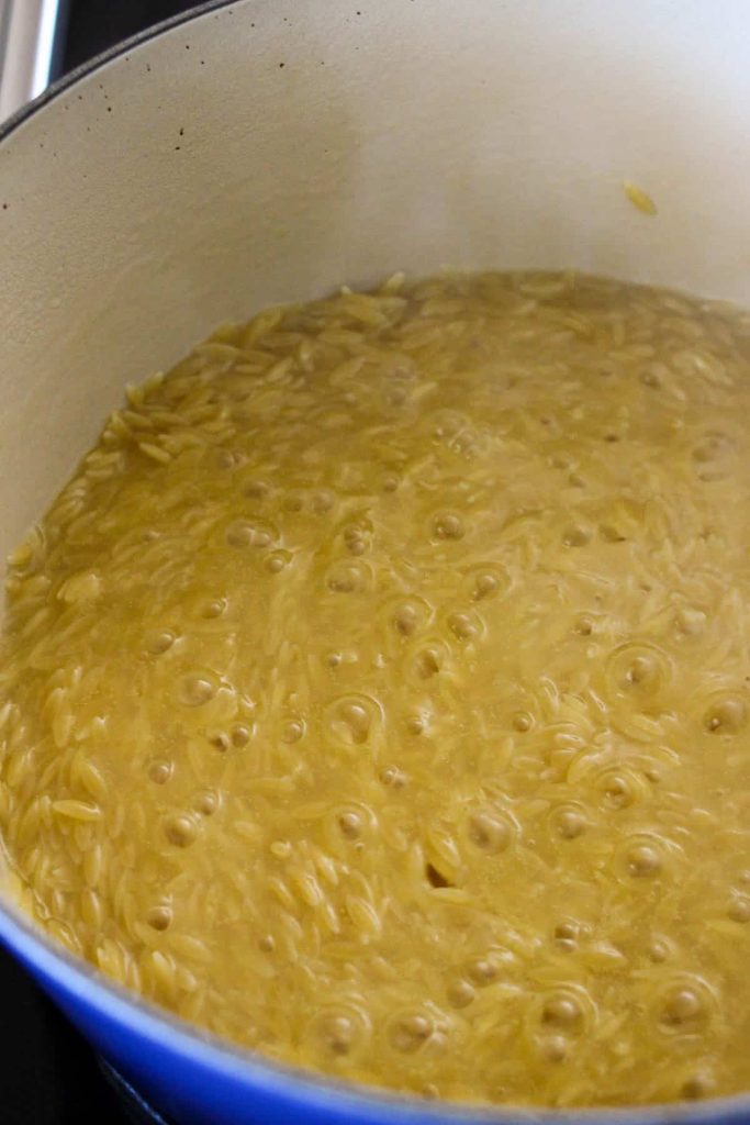 Orzo in a dutch oven simmering in broth. 