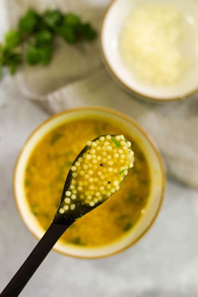 Wooden spoon with soup on it and the bowl of soup in the background. 