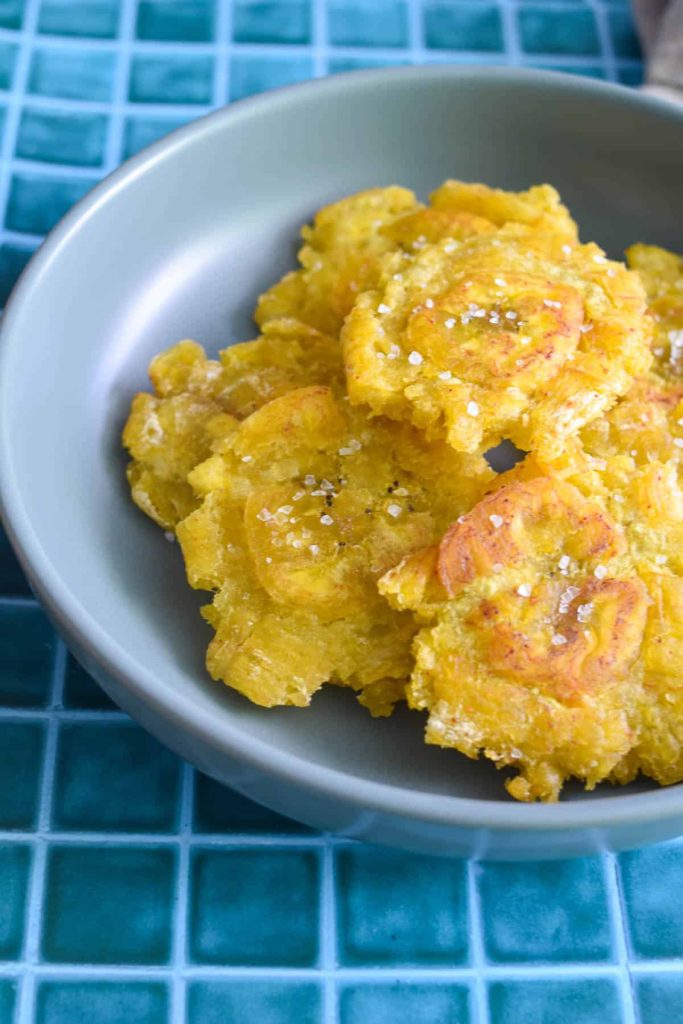 Patacones stacked on top of each other and served in a shallow grey bowl. 