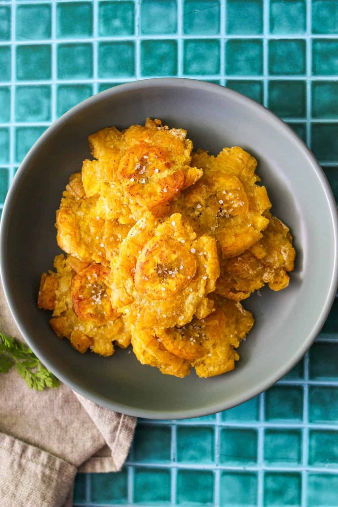 Overhead shot of patacones in a grey bowl on a blue tile background. 