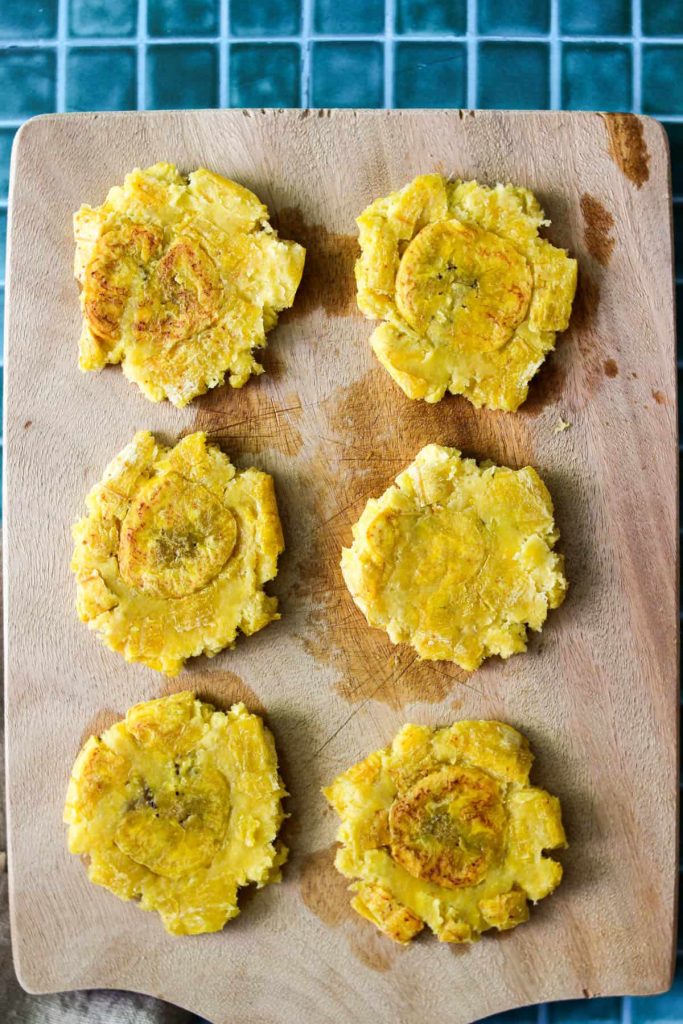 Smashed pieces of plantain on a cutting board. 