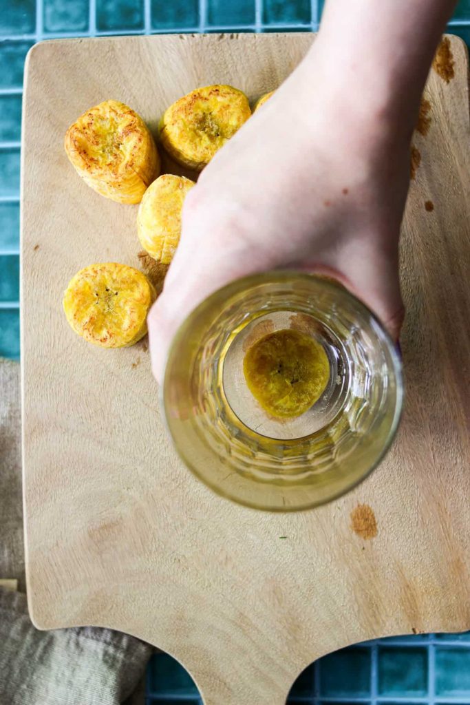 Hand holding a glass on top of a chunk of plantain to smash it. 