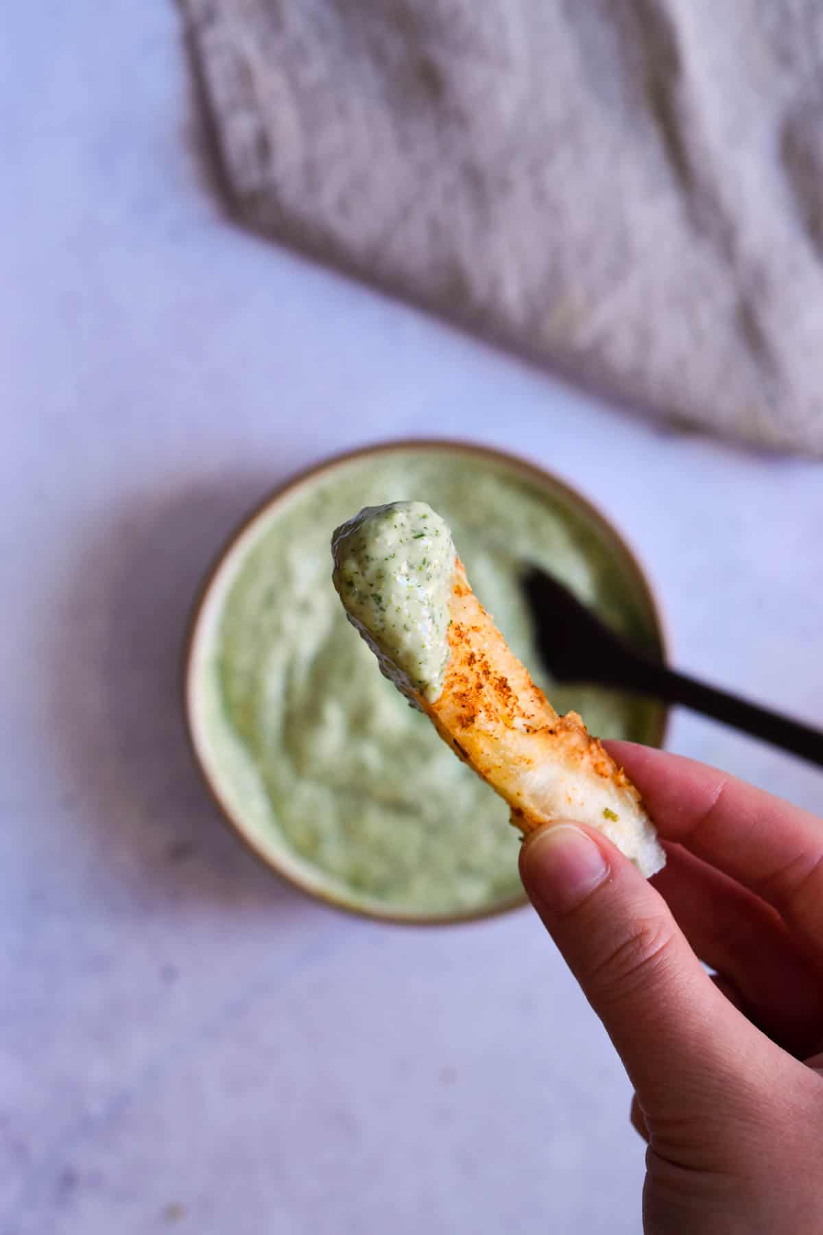 Hand holding up a yuca fry dipped in green sauce to the camera. 