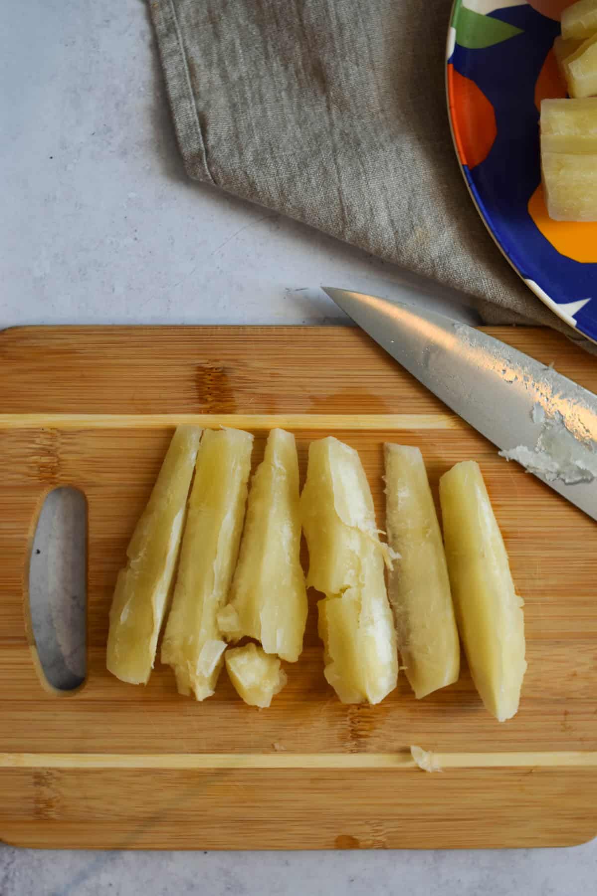 Yuca cut into wedges on a cutting board next to a sharp knife. 