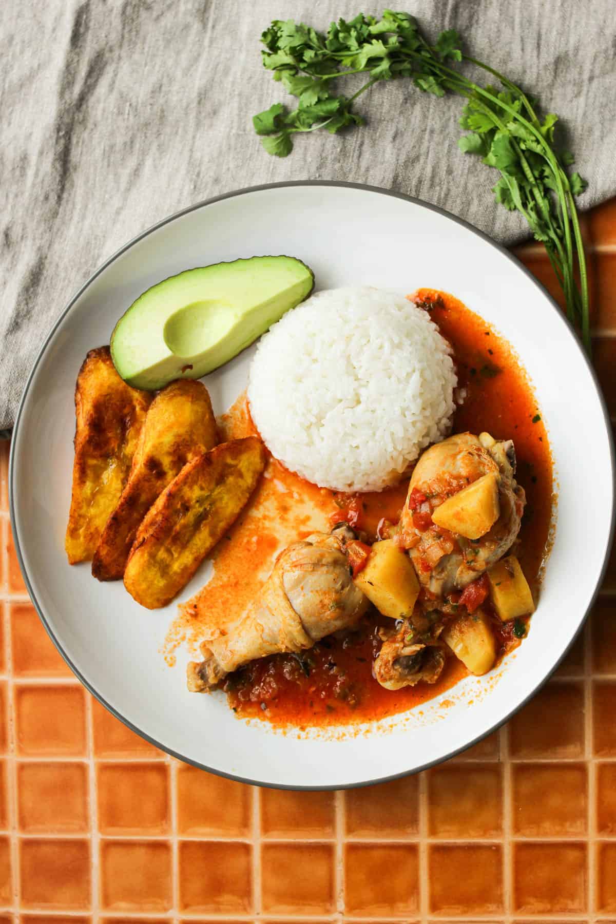 Overhead shot of seco de pollo served on a plate with fried plantains, avocado and rice. 