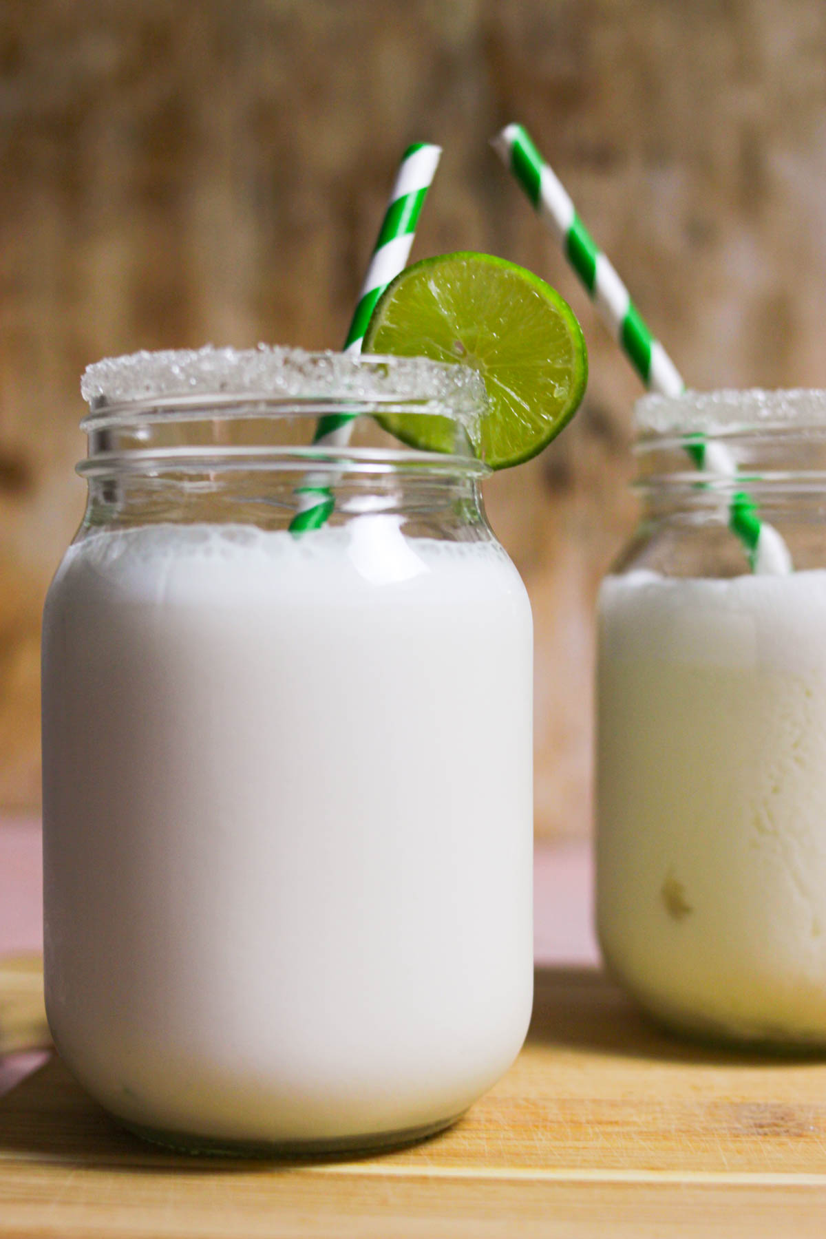 Two jars of limonada de coco with a sugar rim and slice of lime on top. 