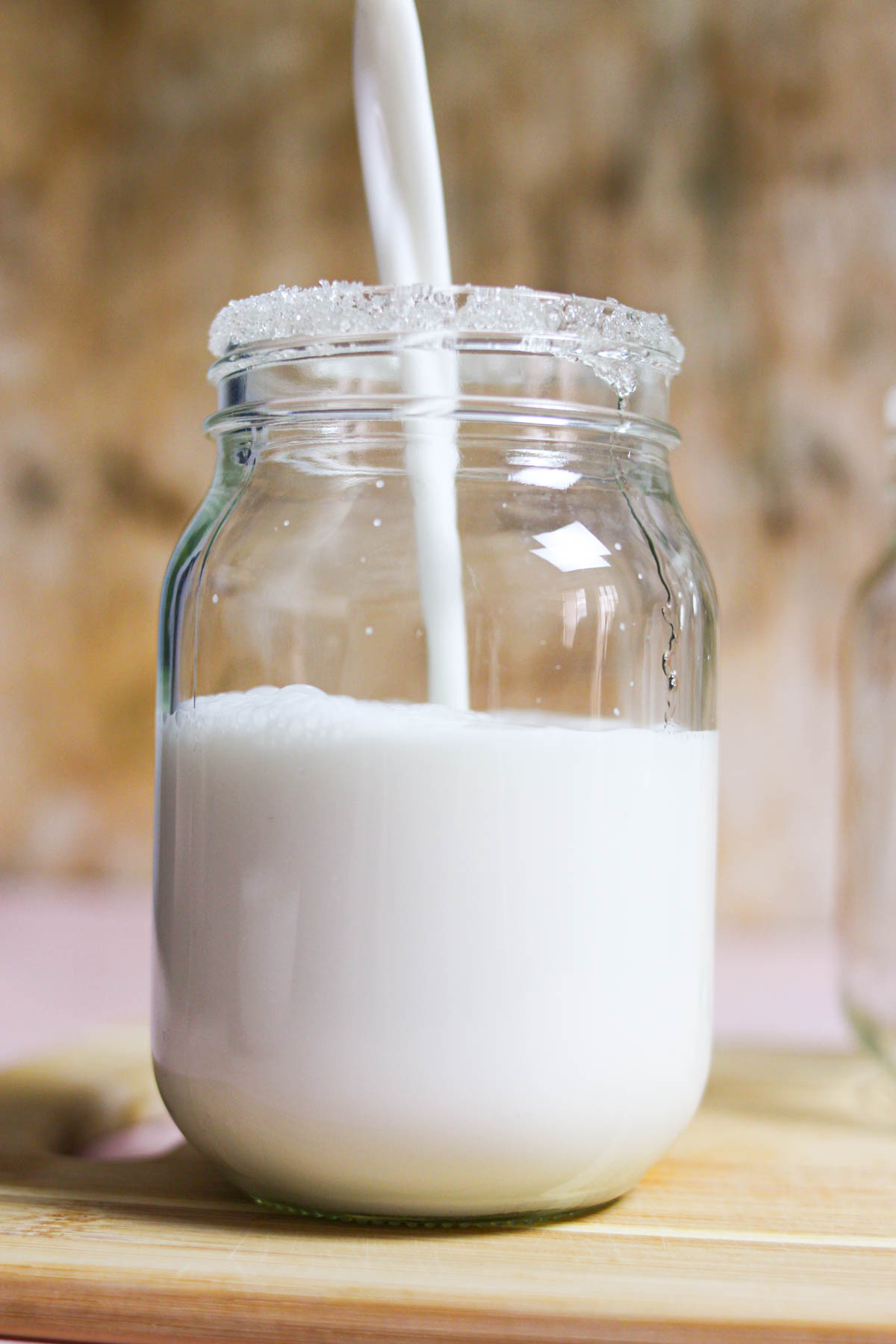 Pouring coconut limeade into a jar with a sugar rim. 