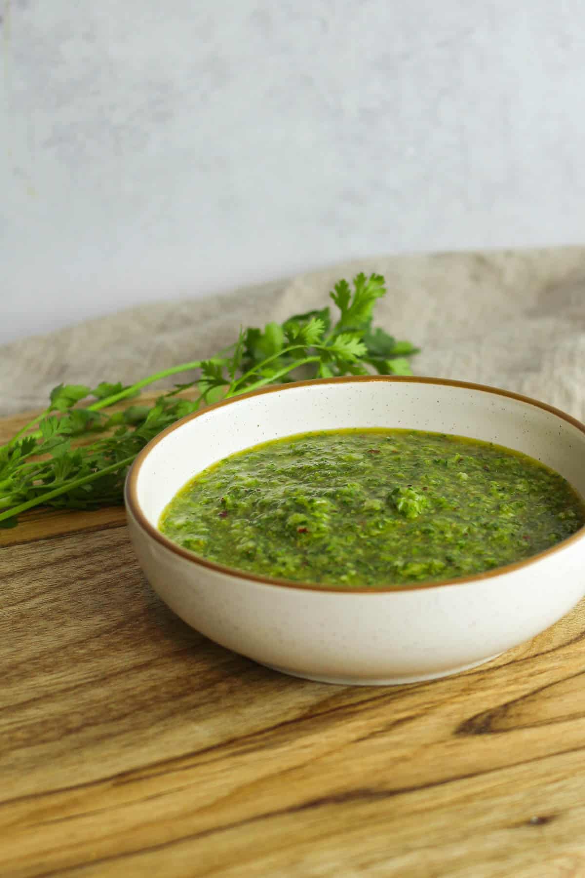 Chimichurri in a bowl on a wooden background with sprigs of cilantro in the background.