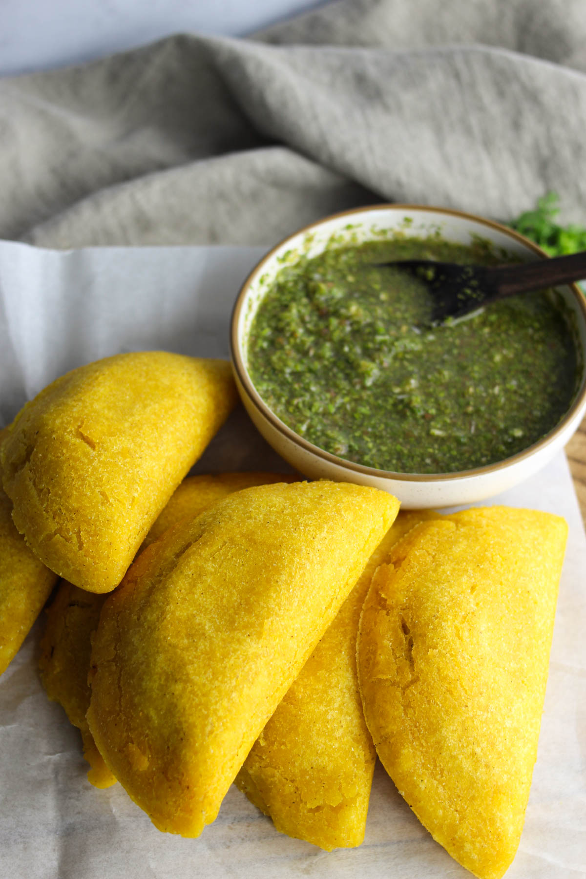 Fried Colombian empanadas stacked on top of each other and served next to a small bowl of sauce. 