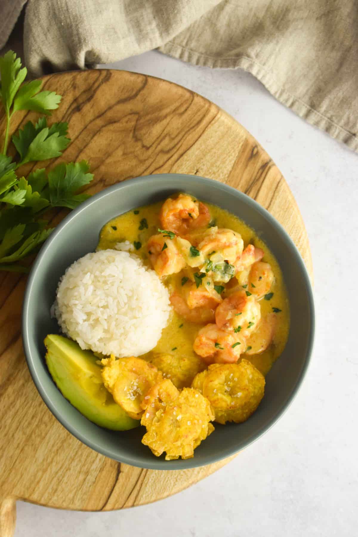 Overhead shot of garlic shrimp served in a blue bowl with rice, plantains and avocado.