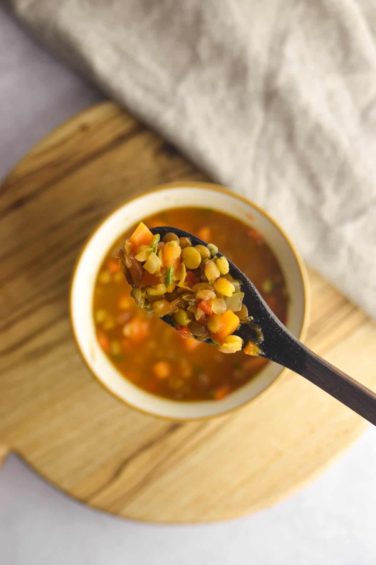 Spoon scooping up carrot and lentil soup with more soup in a bowl below it.