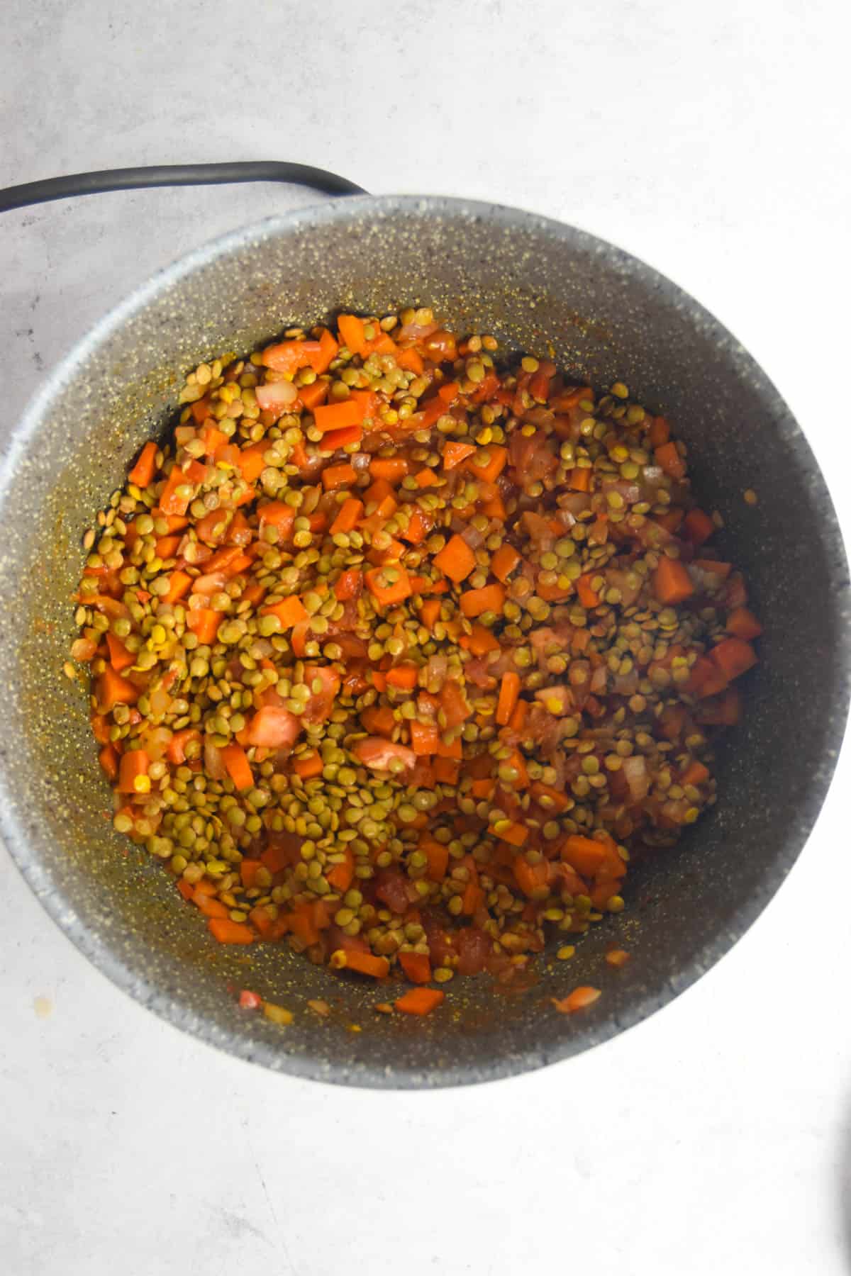 Lentils added to the vegetable mixture in a soup pot.