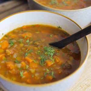 Carrot and lentil soup served in a white bowl with cilantro sprinkled on top.