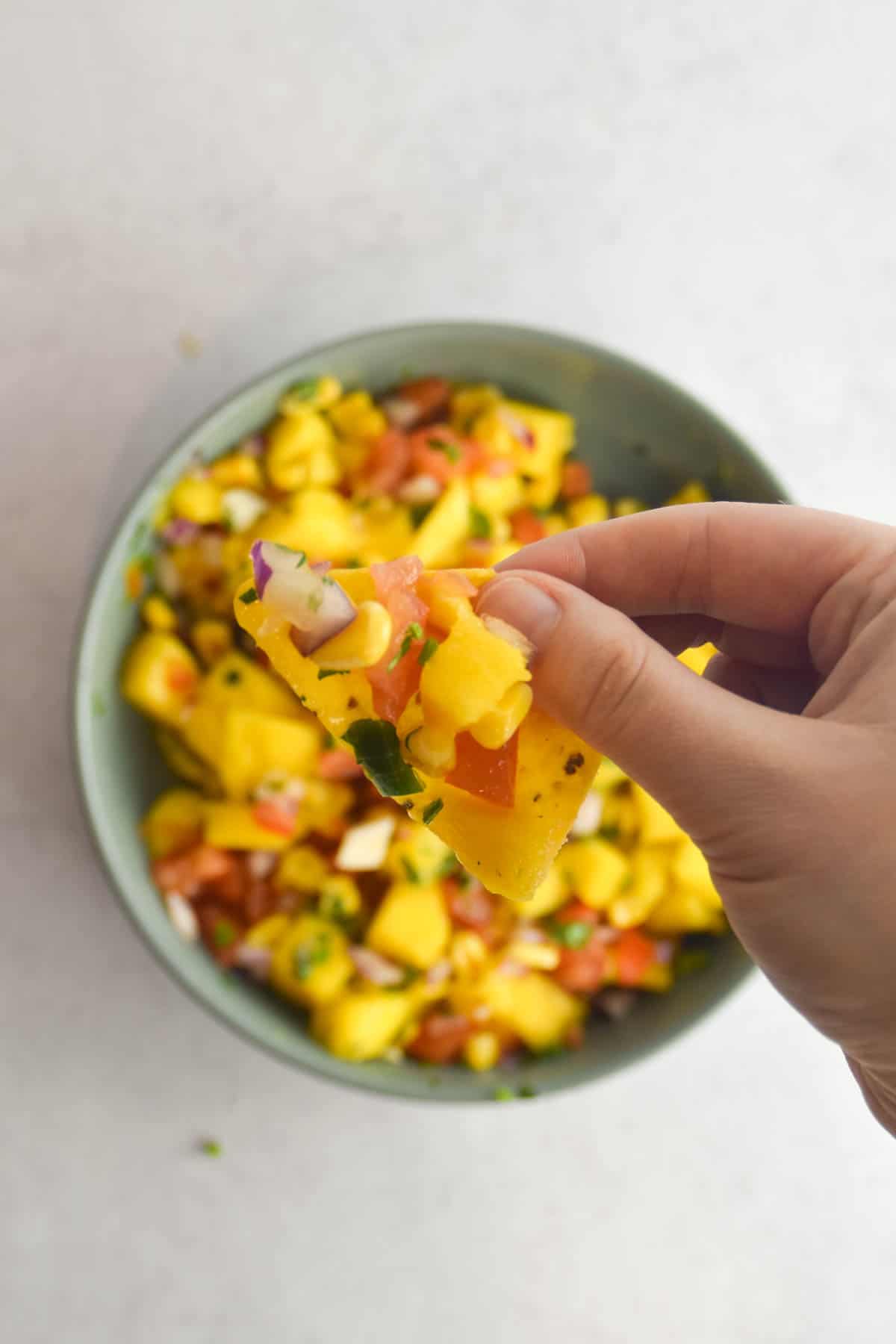 Hand holding a tortilla chip with corn mango salsa on it.