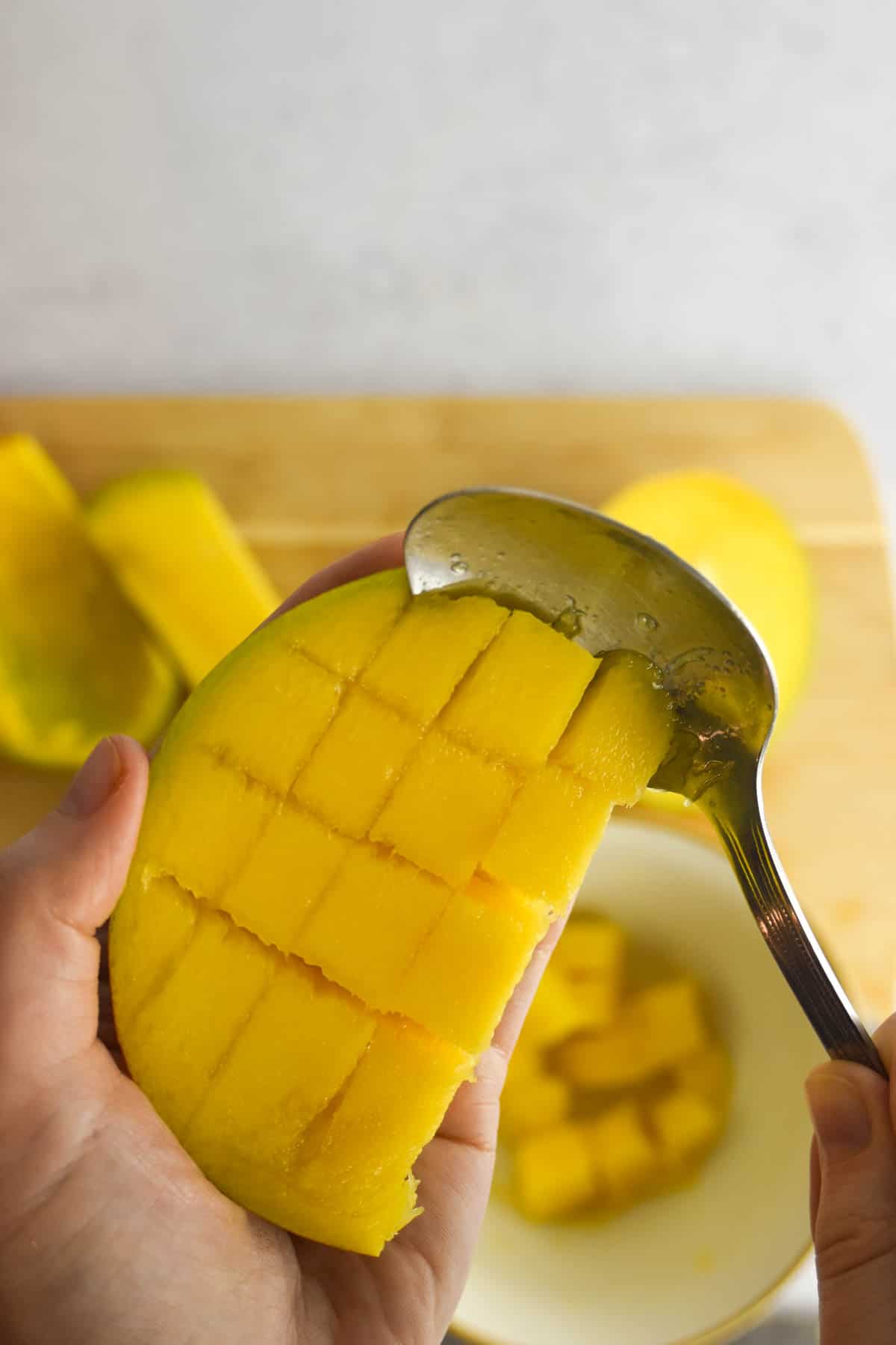 Piece of mango sliced into squares with a spoon scooping the mango flesh from the peel.