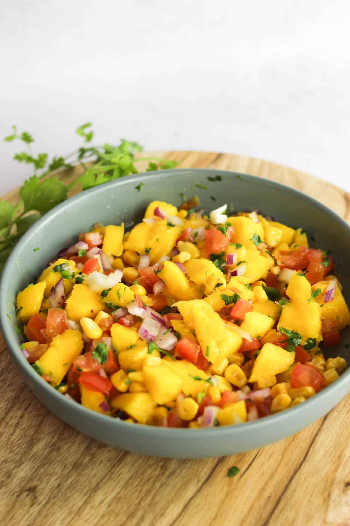 Side view of corn mango salsa served in a blue bowl on a wooden background.