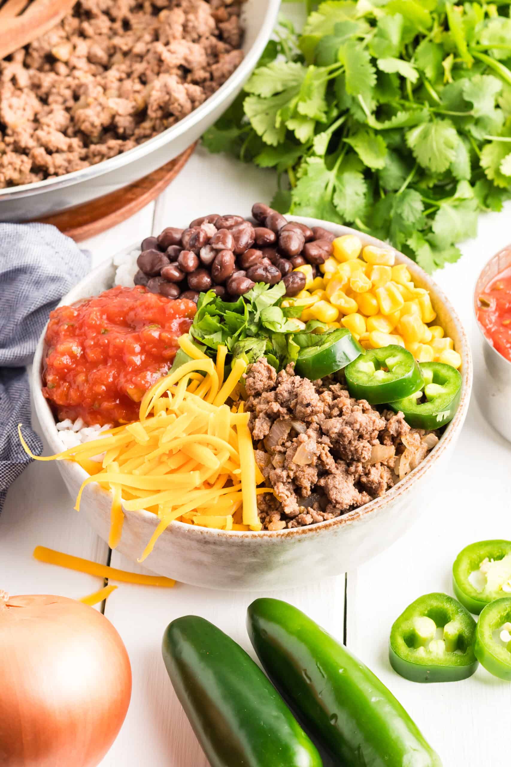 Loaded taco bowl served in a bowl surrounded by ground beef, cilantro, and jalapeños.