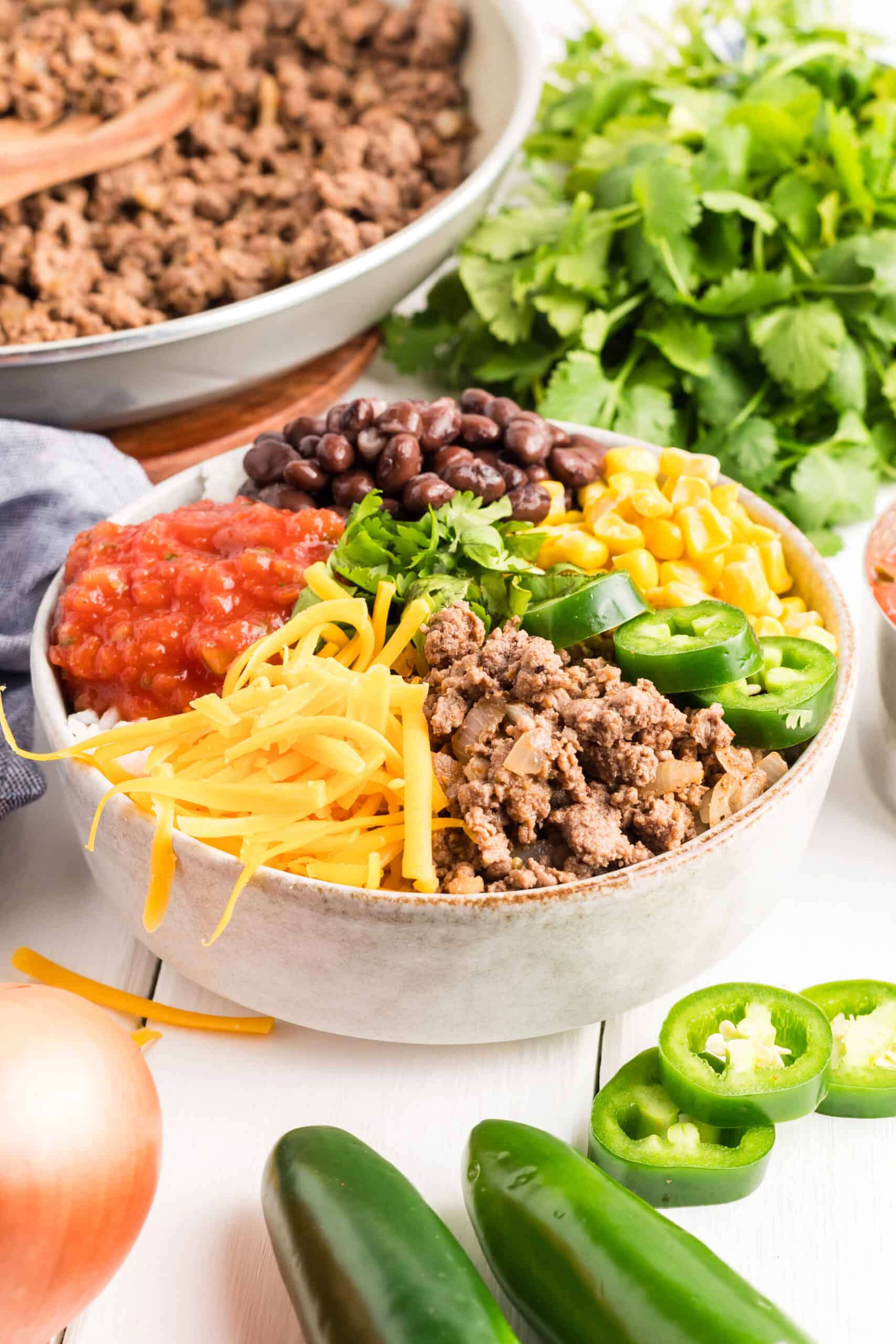 Assembled taco bowl with ground beef and cilantro in the background.