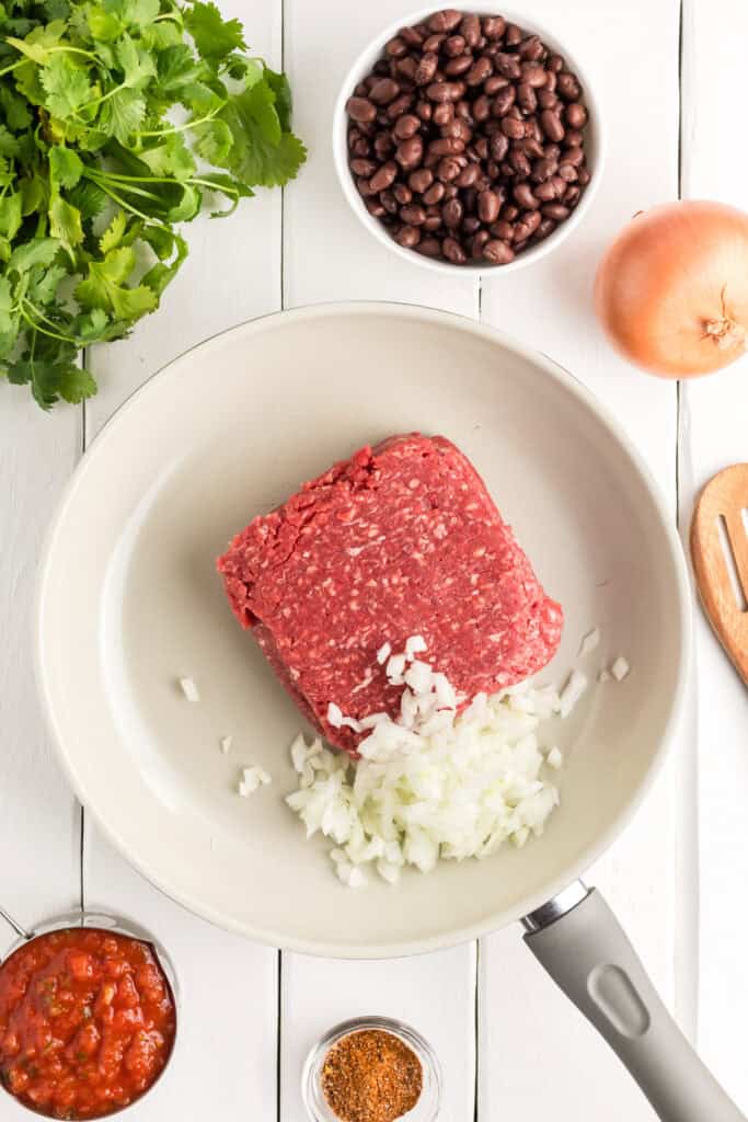 Ground beef and diced onion in a skillet.