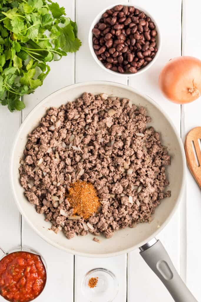 Ground beef and onions in a skillet with seasoning added.