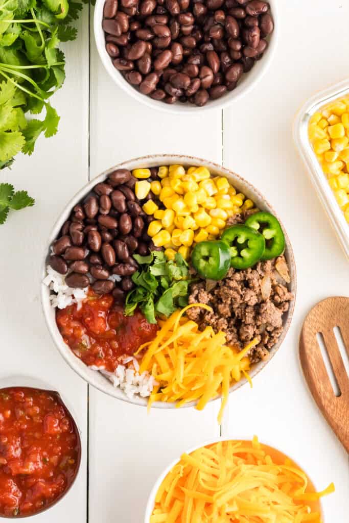 Taco bowl assembled with salsa, cheese, beef, beans, corn and jalapeños.