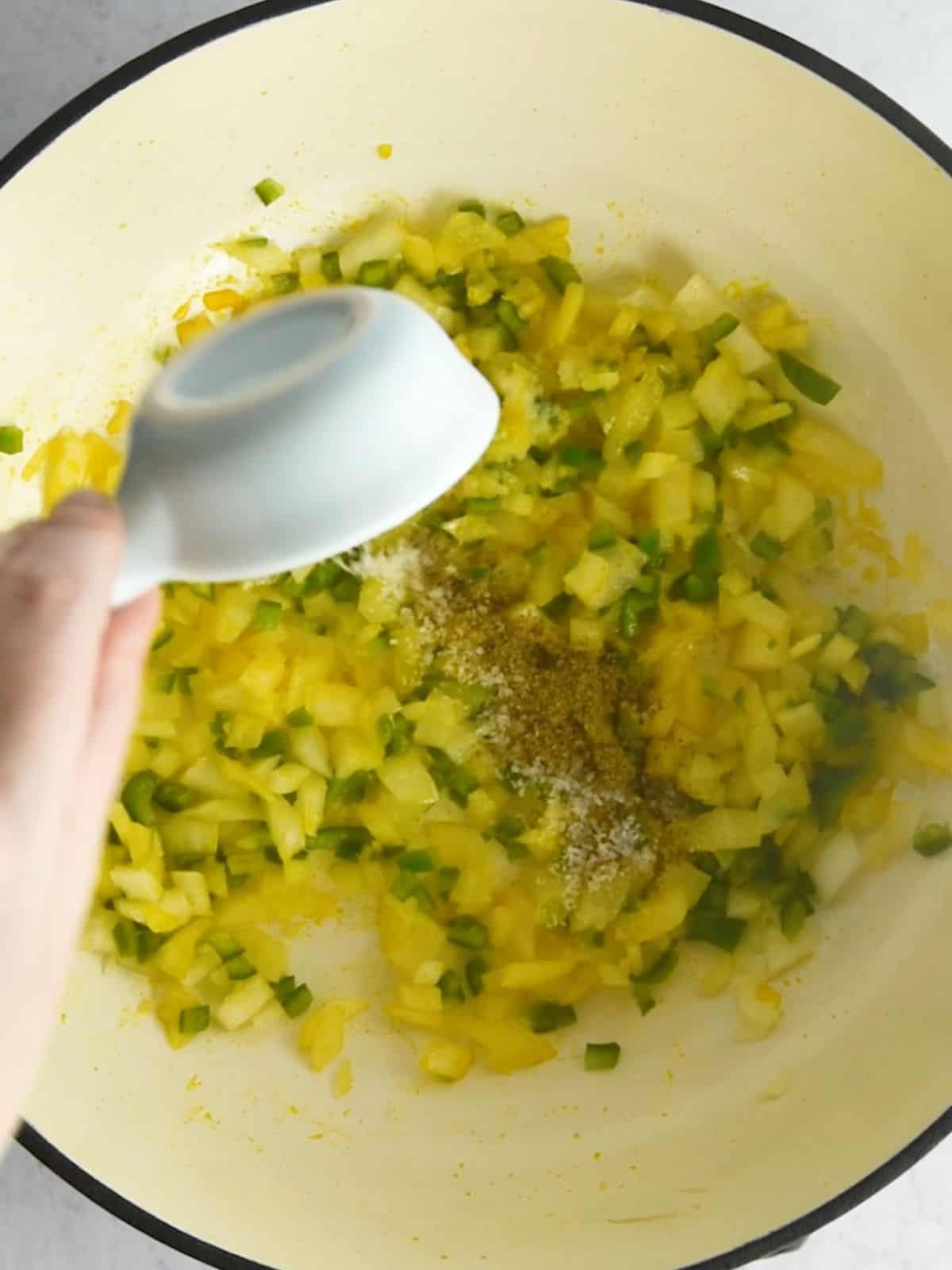 Onion and green peppers cooking in a pot with cumin added.