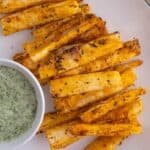 Crispy air fryer yuca fries on a plate next to a green sauce.