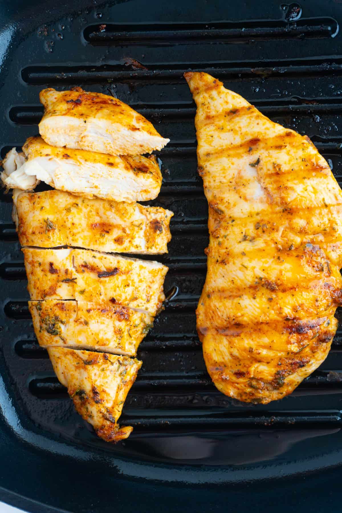 Two chicken breasts in a cast iron pan with one in slices.