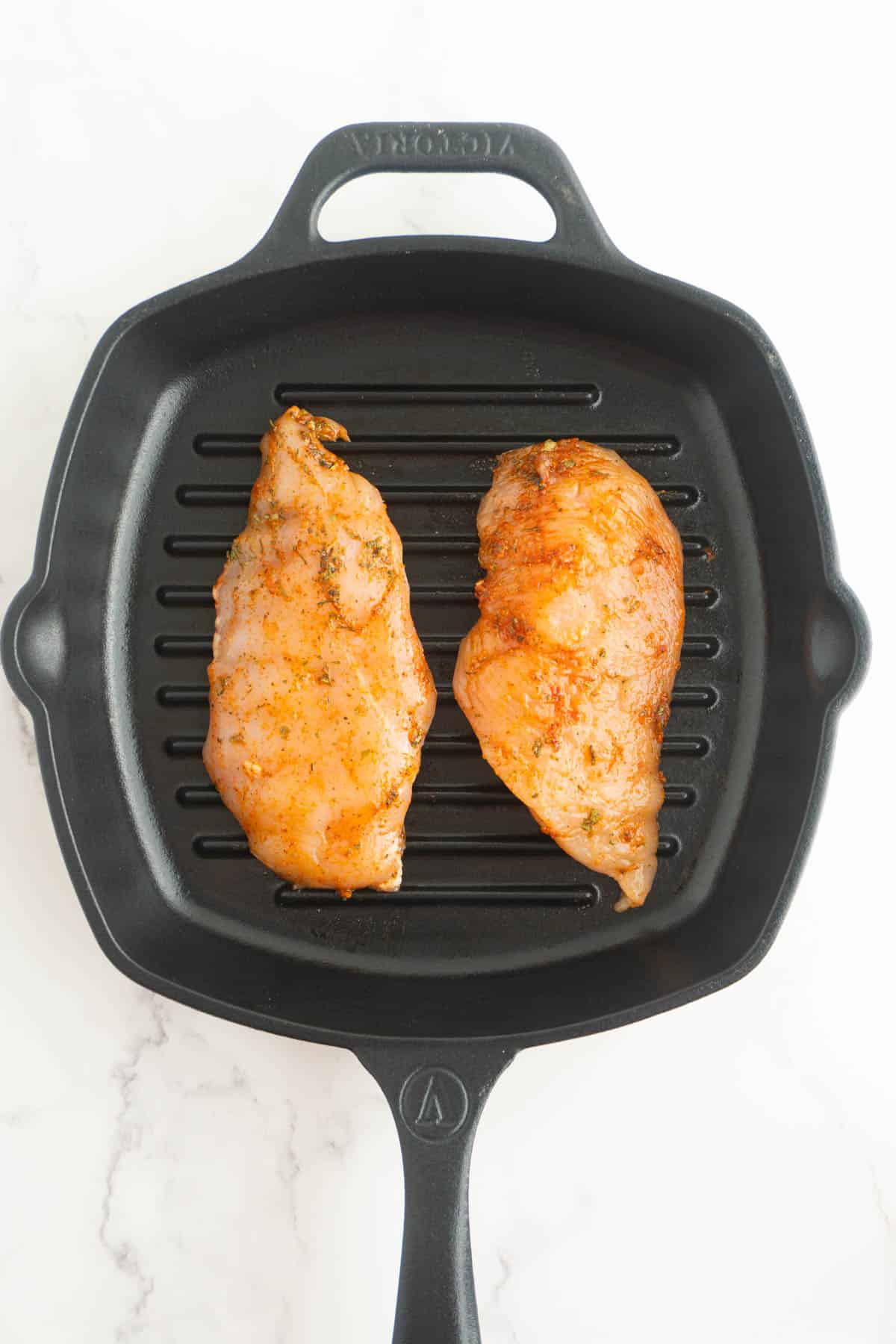 Seasoned chicken breasts in a cast iron skillet.