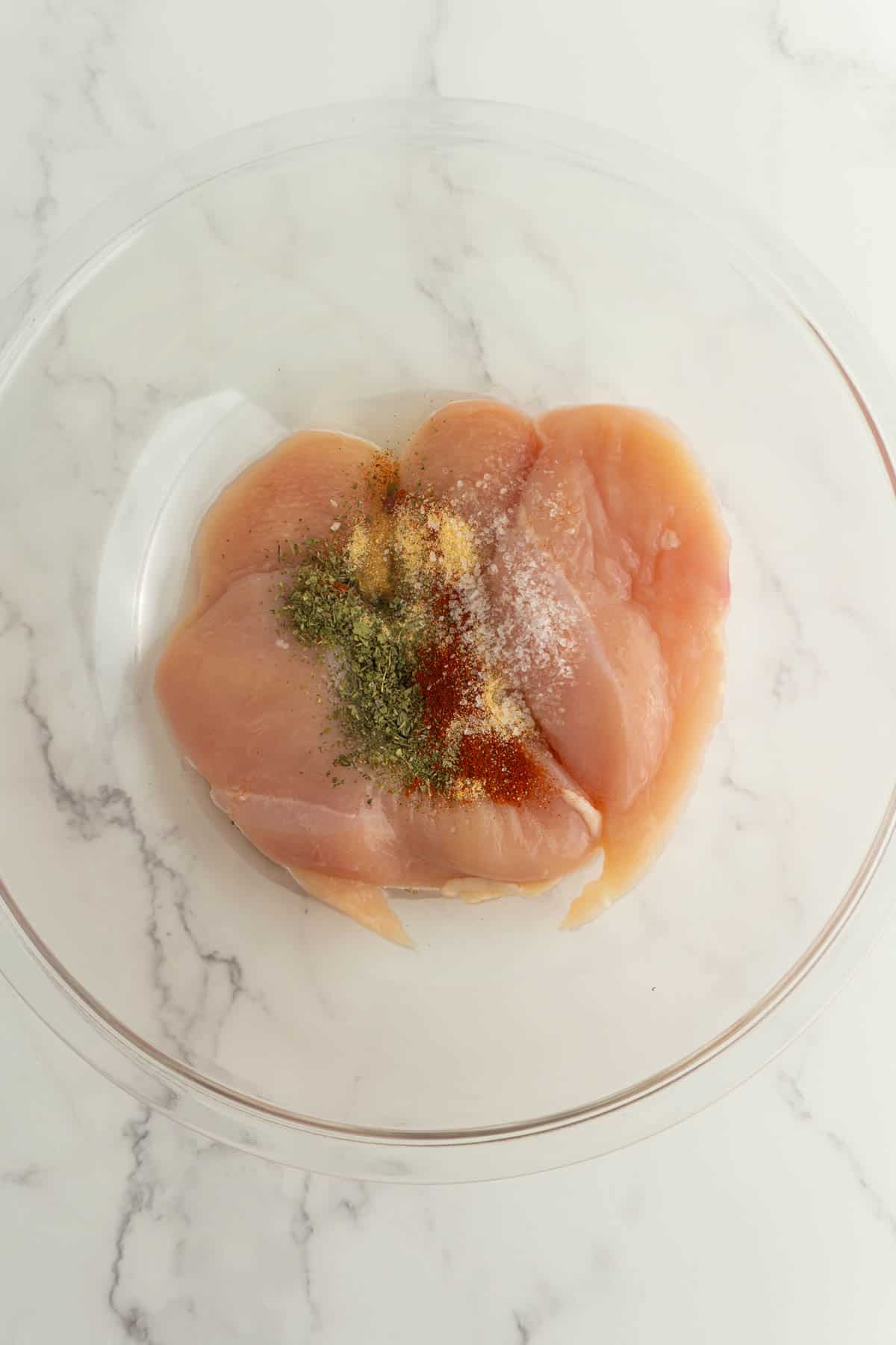 Chicken breasts with seasonings on top before being mixed together.