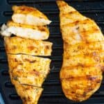 Two pieces of chicken breast in a cast iron with one of them sliced.