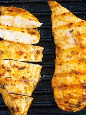 Two pieces of chicken breast in a cast iron with one of them sliced.