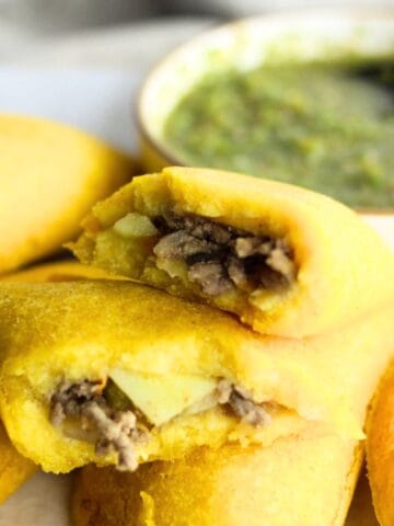 Colombian empanada broken in half to show filling and placed on top of other empanadas.