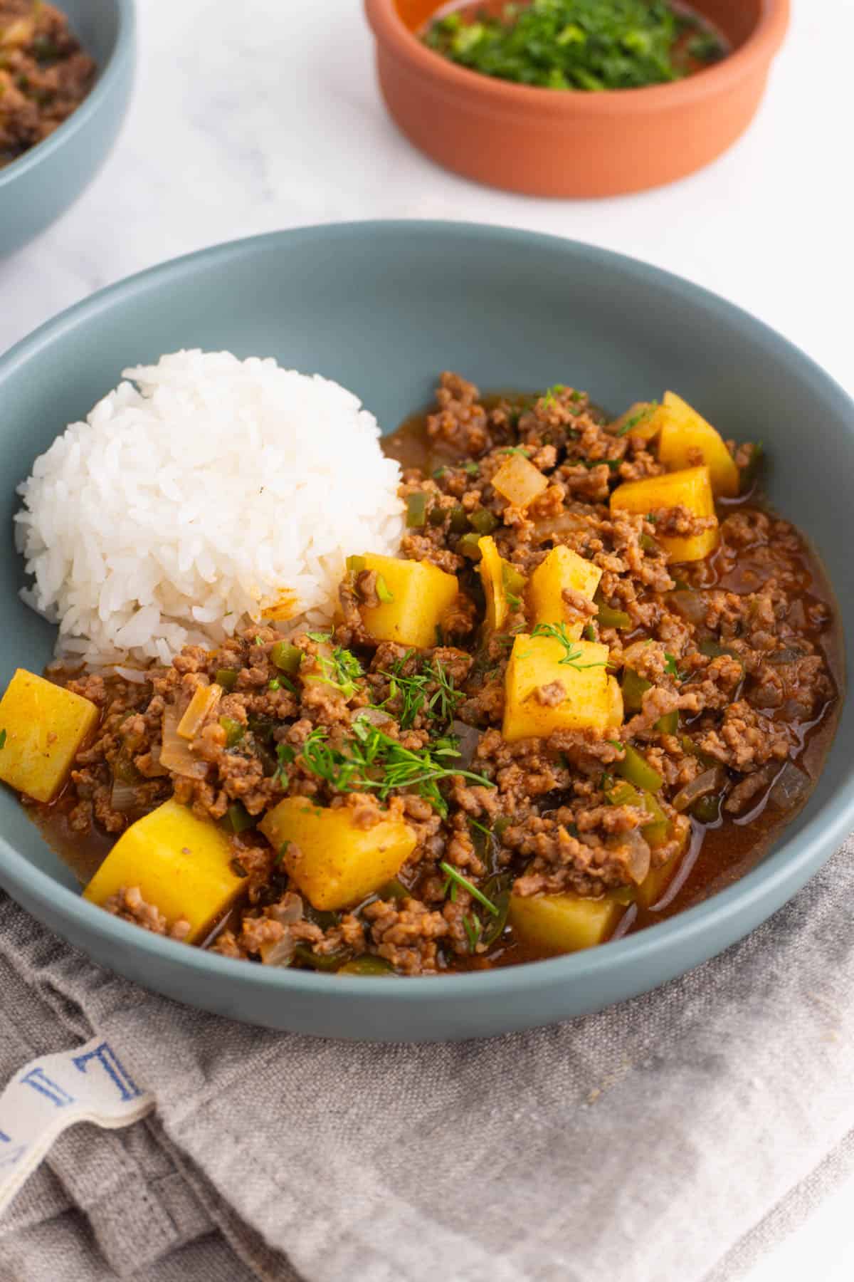 Mexican picadillo with potatoes served in a grey bowl with a side of rice.